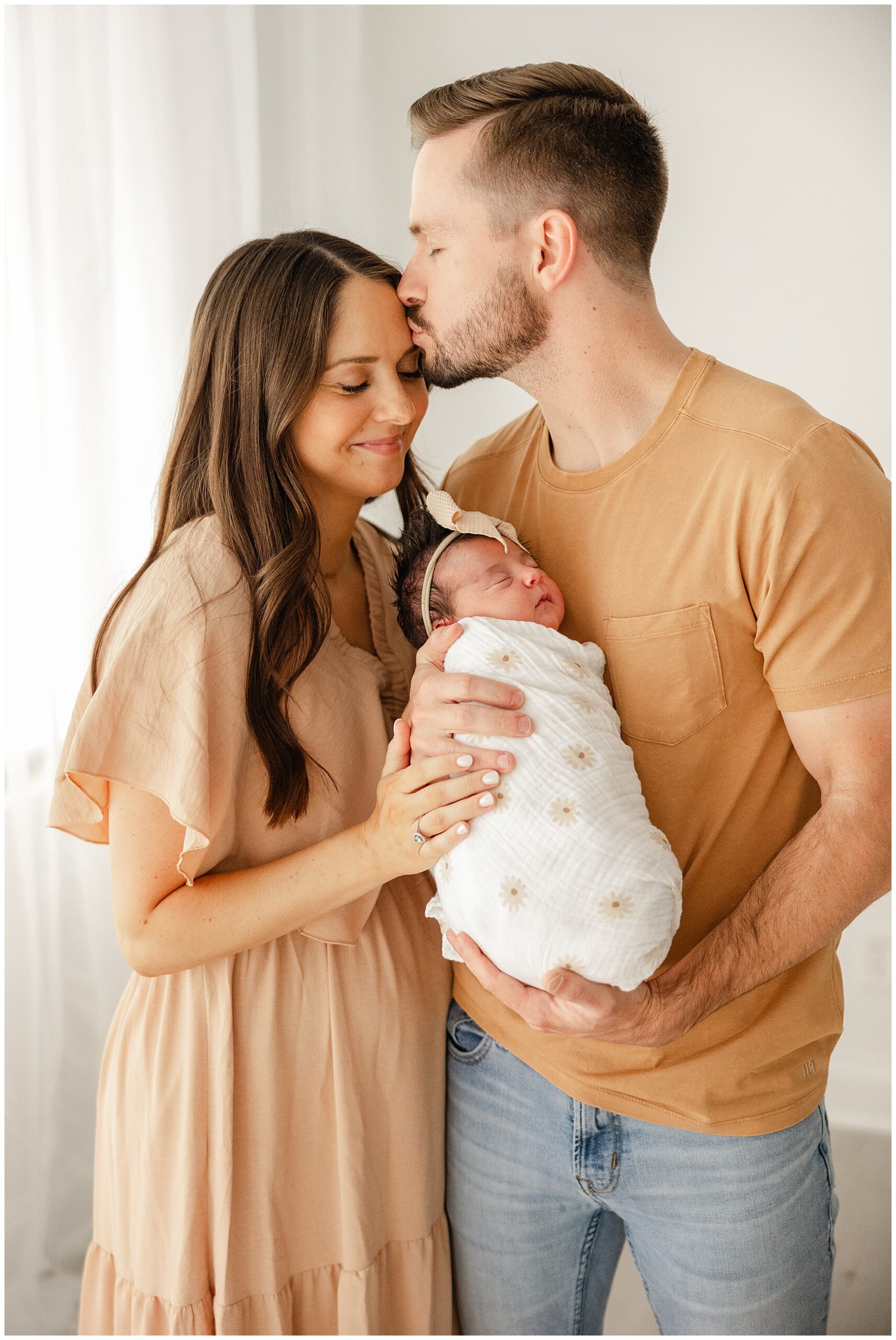 dad holding newborn baby and kissing mom's forehead
