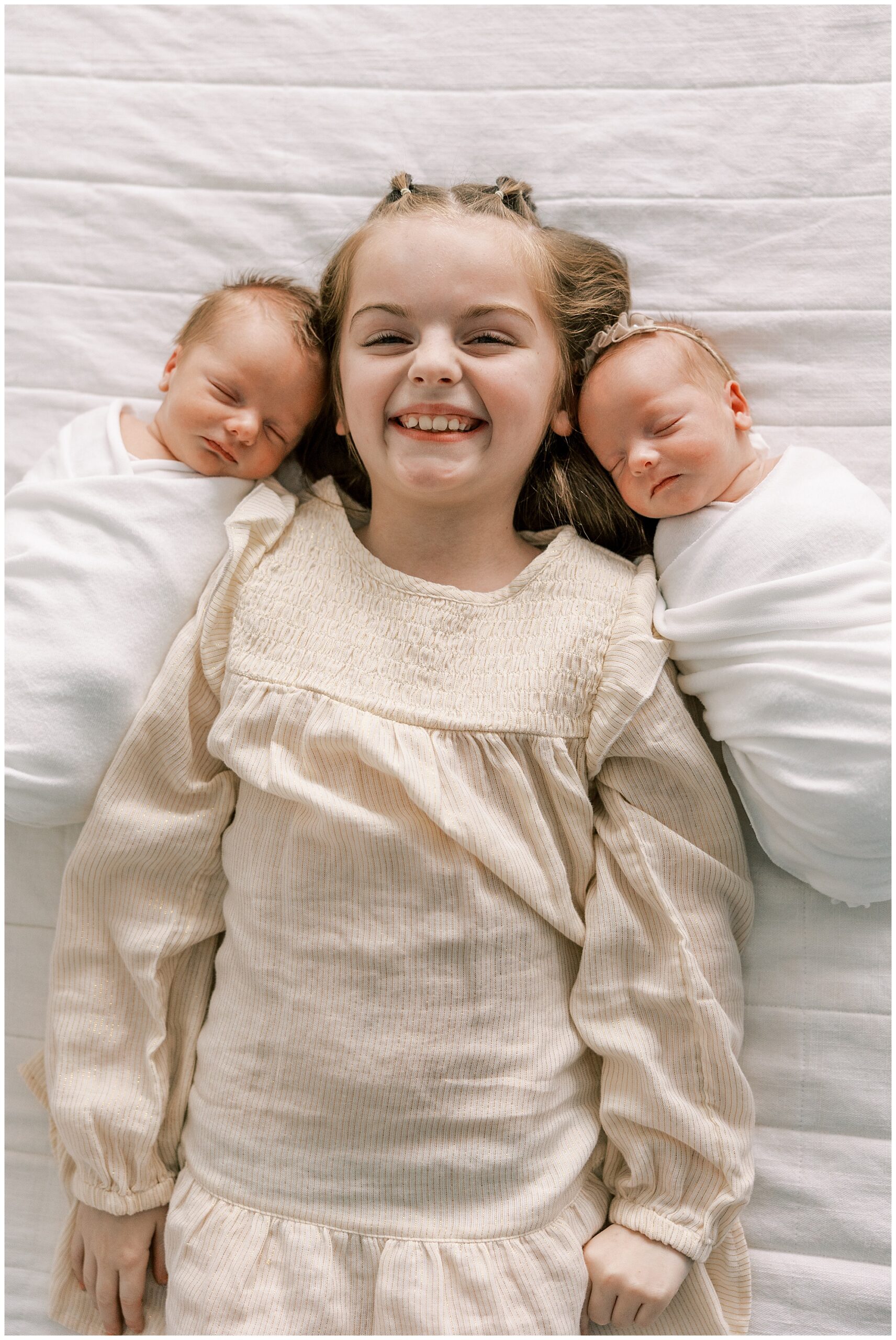 big sister laying with twin newborn siblings