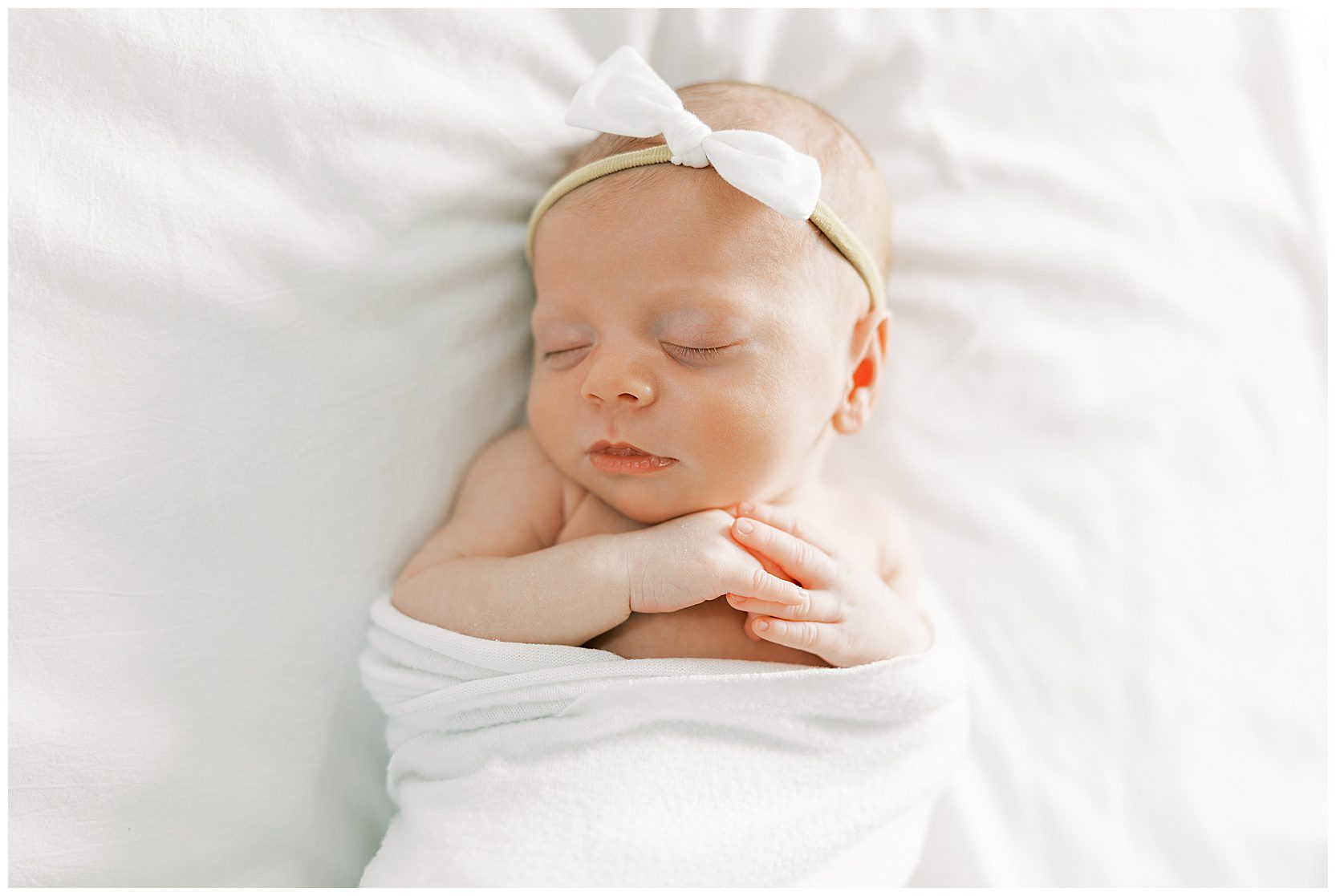 newborn with hands folded on bed