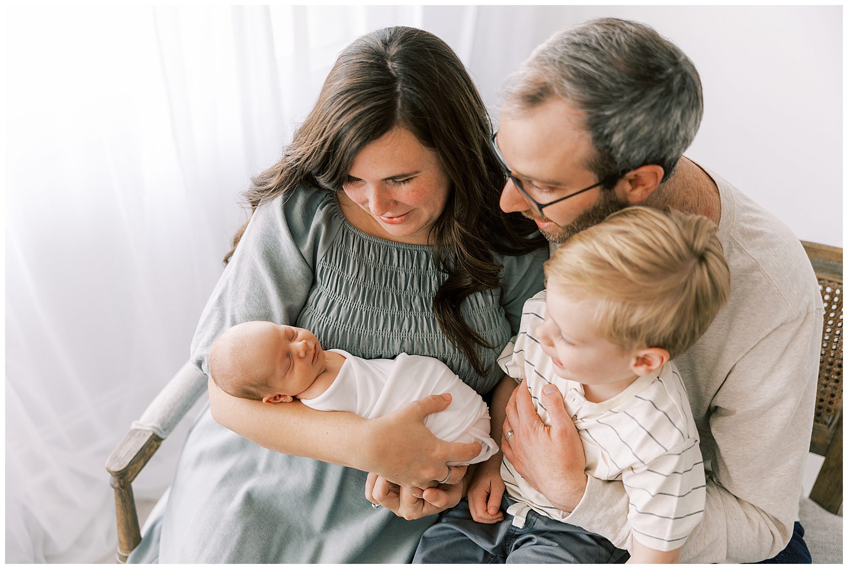whole family sitting on bench looking at newborn baby
