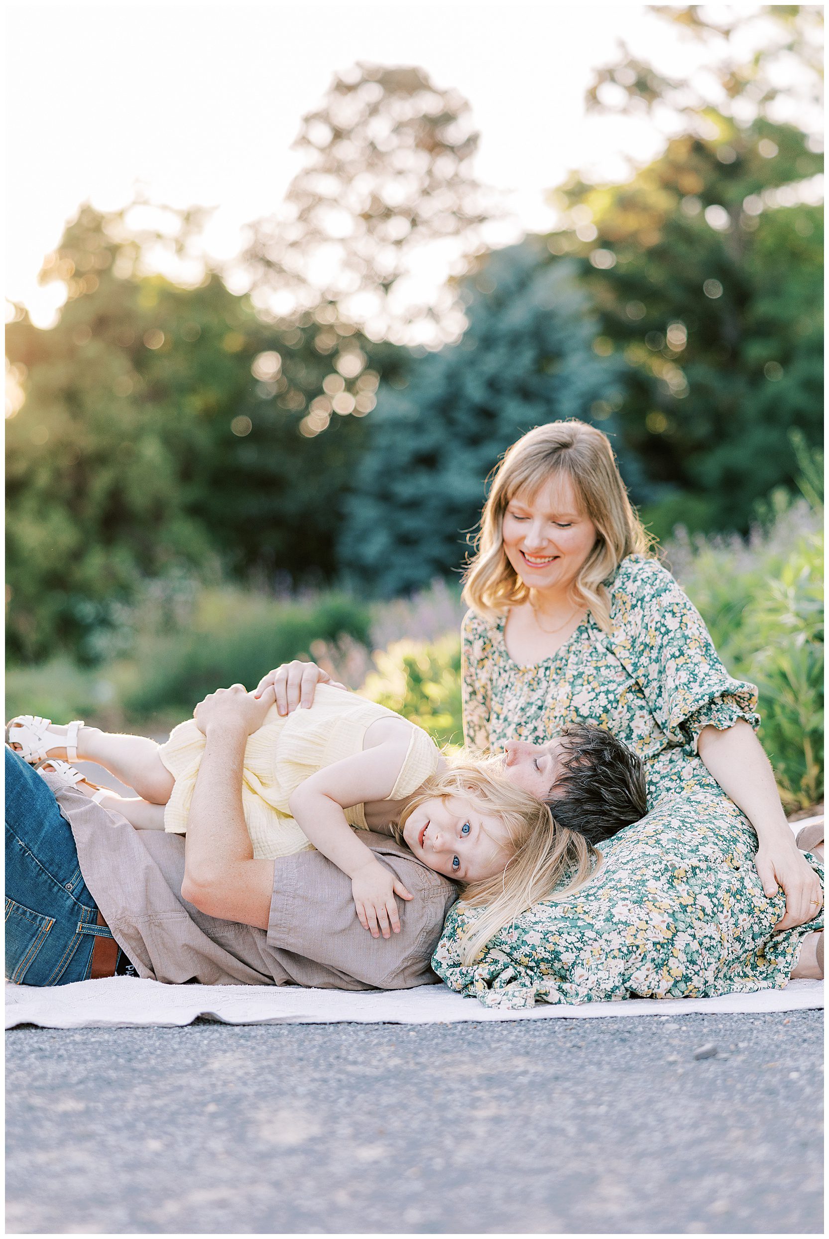 mom, dad and daughter laying on blanket at gardens