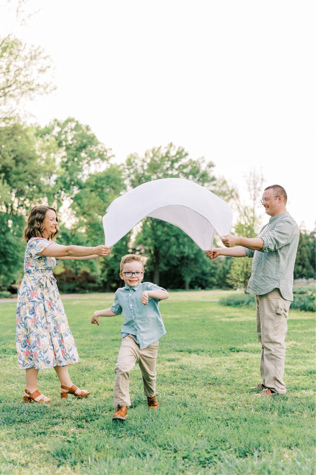 boy running underneath blanket that mom and dad are tossing up 