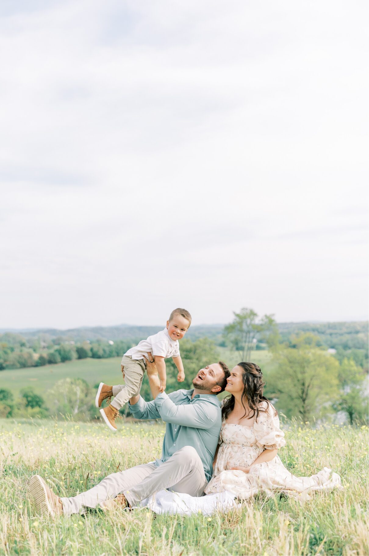 family sitting down on blanket holding little boy in air